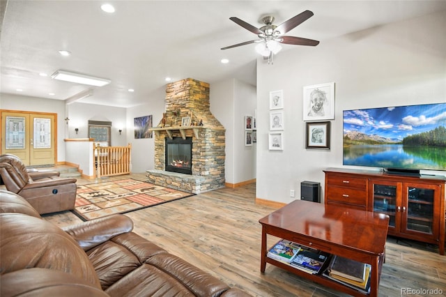 living room with wood-type flooring, a stone fireplace, and ceiling fan