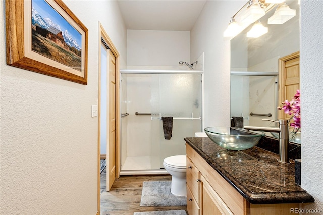 bathroom with wood-type flooring, vanity, toilet, and a shower with shower door