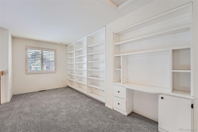 unfurnished office with light colored carpet, built in shelves, and built in desk