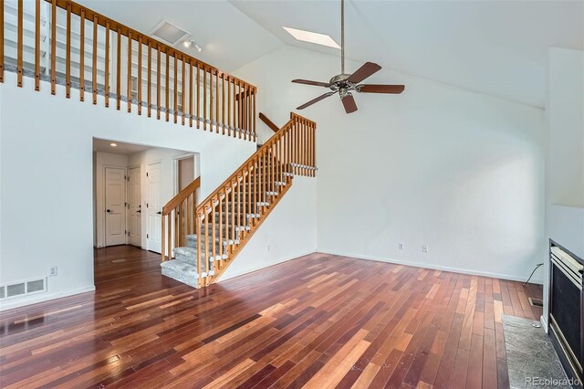 unfurnished living room featuring high vaulted ceiling, dark wood-type flooring, a skylight, and ceiling fan