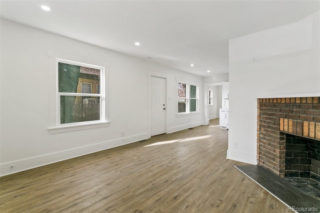 unfurnished living room with wood-type flooring and a brick fireplace