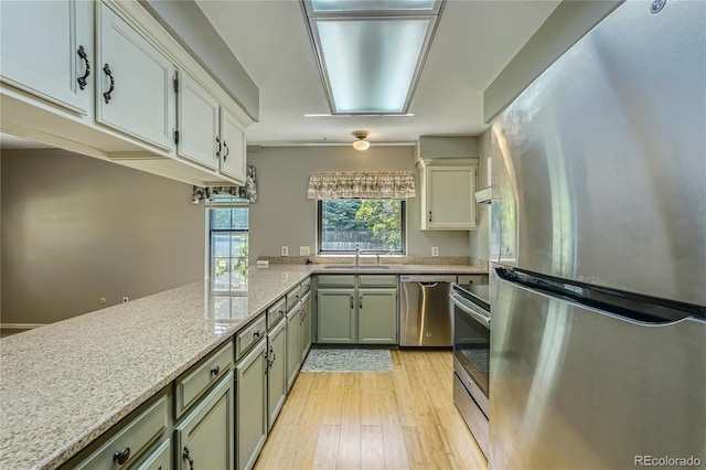 8164 Flower Cir, Arvada, CO 80005 - kitchen with stainless steel appliances, a sink, light wood-style flooring, light stone counters, and a peninsula