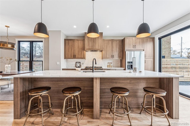 kitchen with a large island with sink, a kitchen breakfast bar, decorative backsplash, decorative light fixtures, and high end fridge