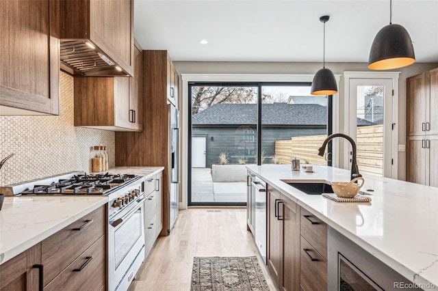 kitchen featuring backsplash, custom exhaust hood, gas range, sink, and hanging light fixtures