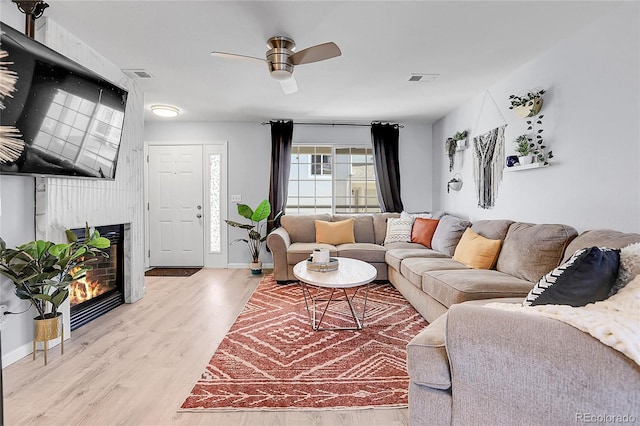 living area with light wood finished floors, a large fireplace, visible vents, baseboards, and ceiling fan