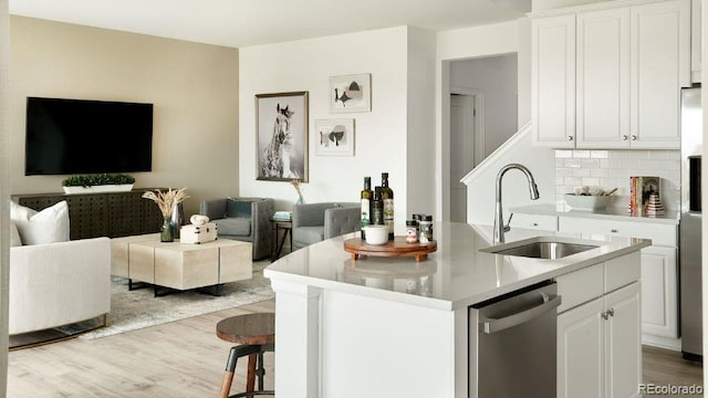 kitchen with white cabinets, dishwasher, an island with sink, sink, and backsplash