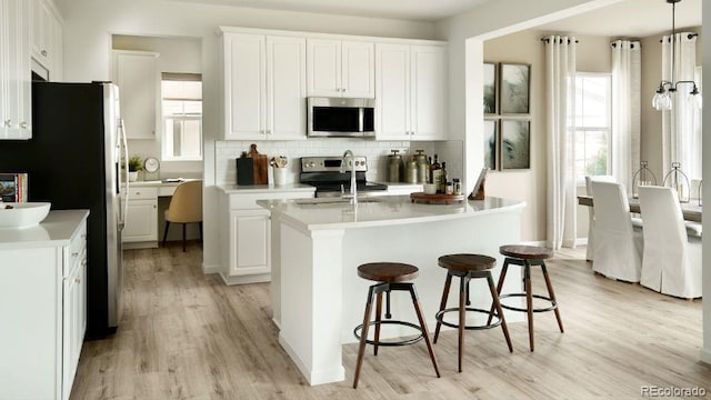 kitchen with stainless steel appliances, pendant lighting, light hardwood / wood-style floors, and white cabinetry