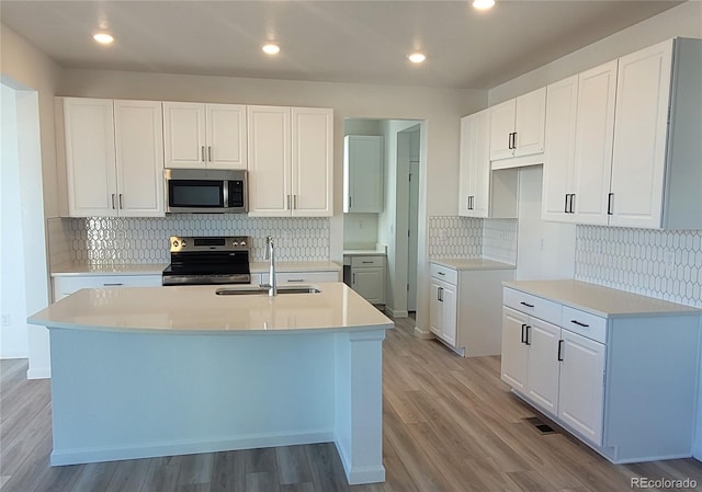 kitchen with white cabinets, stainless steel appliances, a kitchen island with sink, and sink