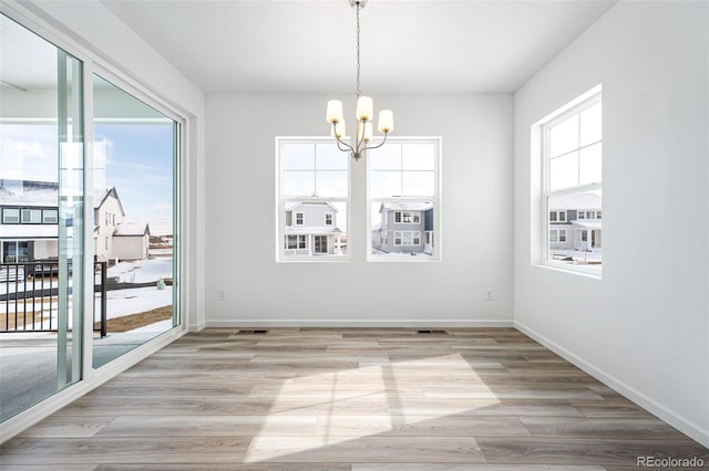 unfurnished dining area with light wood-type flooring, an inviting chandelier, visible vents, and baseboards