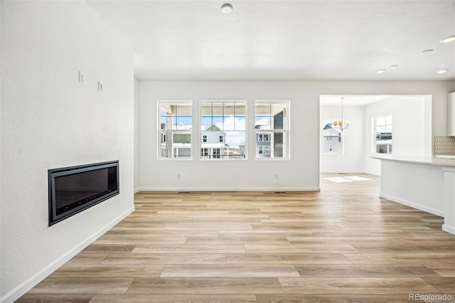 unfurnished living room featuring a chandelier, recessed lighting, baseboards, light wood-style floors, and a glass covered fireplace