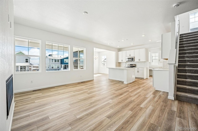 unfurnished living room featuring stairs, recessed lighting, light wood-style flooring, and baseboards