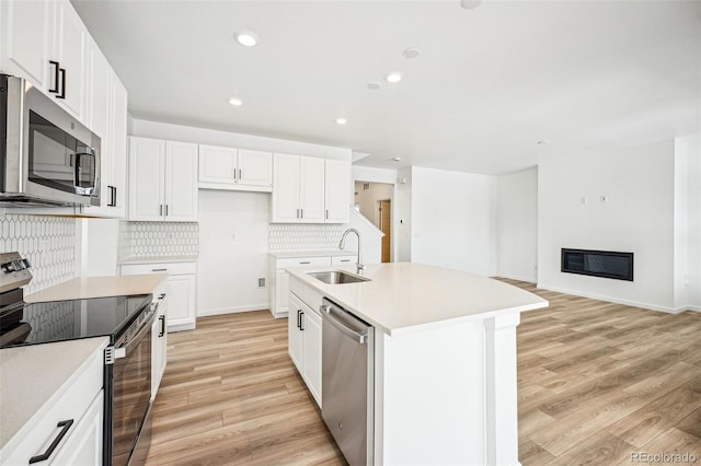 kitchen featuring tasteful backsplash, a glass covered fireplace, light wood-style flooring, stainless steel appliances, and a sink