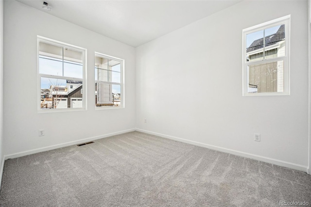 empty room with carpet, visible vents, and baseboards