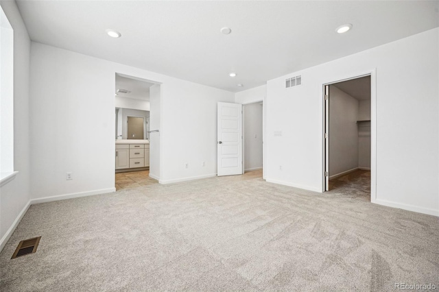 unfurnished bedroom featuring recessed lighting, a walk in closet, visible vents, and light colored carpet