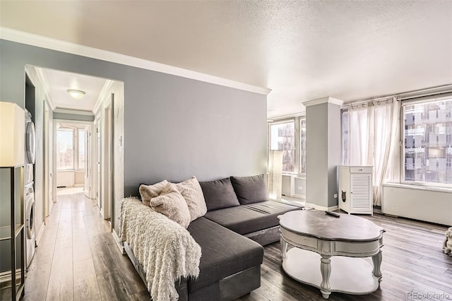 living area with crown molding, wood finished floors, and stacked washing maching and dryer