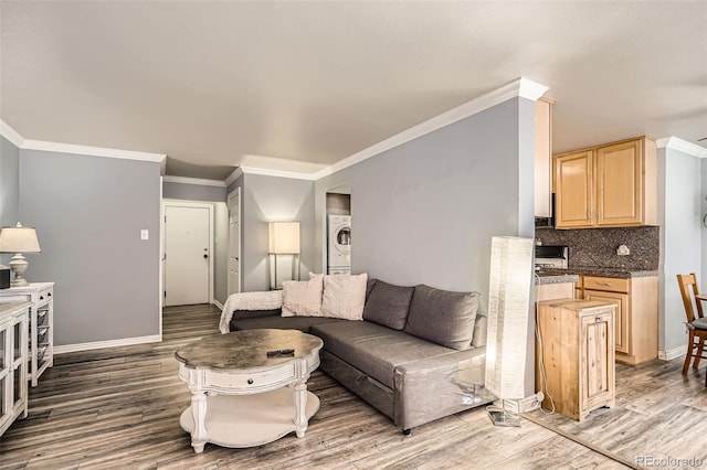 living room featuring stacked washer and dryer, wood finished floors, baseboards, and ornamental molding