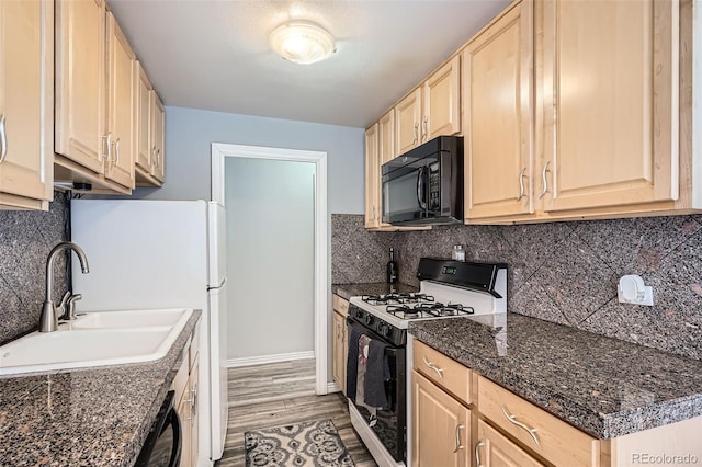 kitchen featuring light wood finished floors, tasteful backsplash, light brown cabinets, black appliances, and a sink