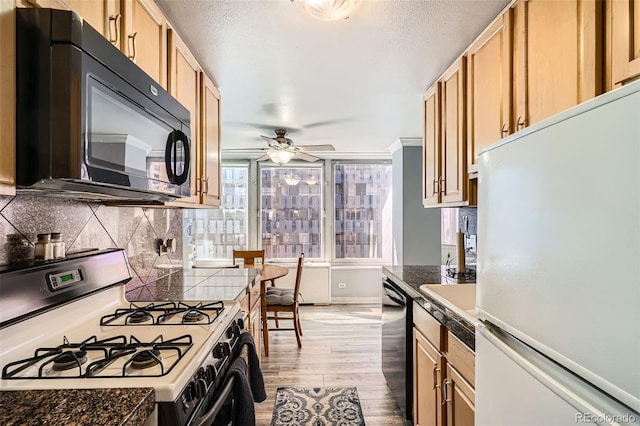 kitchen with light brown cabinets, light wood-style flooring, ceiling fan, black appliances, and backsplash