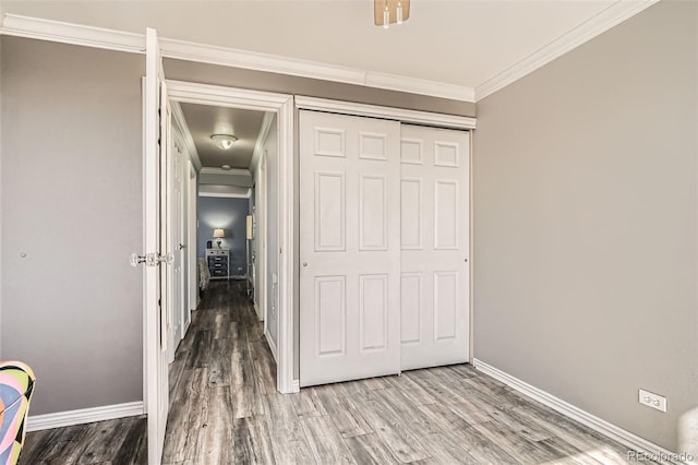 unfurnished bedroom featuring a closet, crown molding, baseboards, and wood finished floors