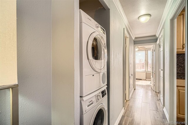 clothes washing area with crown molding, laundry area, stacked washing maching and dryer, light wood-style floors, and a textured wall