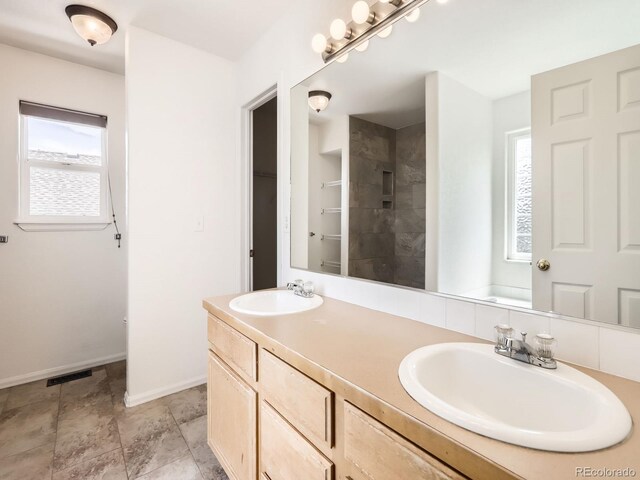 bathroom with healthy amount of natural light, tiled shower, baseboards, and double vanity