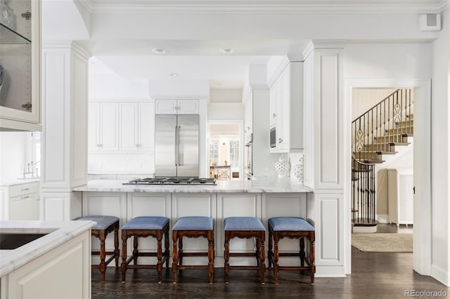 kitchen featuring light stone counters, white cabinetry, stainless steel appliances, and a breakfast bar area