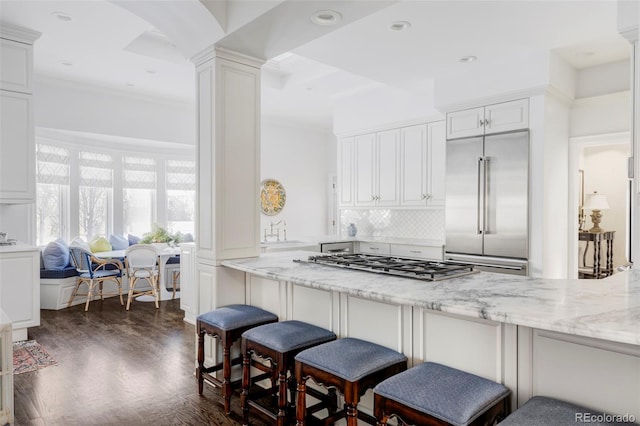 kitchen featuring stainless steel appliances, white cabinetry, a kitchen bar, and light stone countertops