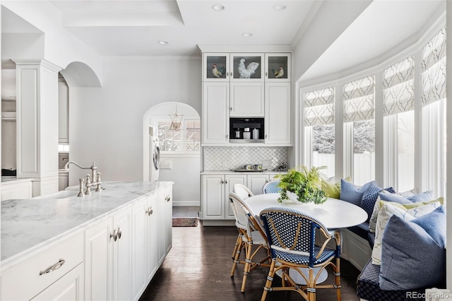 kitchen with dark hardwood / wood-style flooring, backsplash, white cabinetry, light stone countertops, and decorative columns