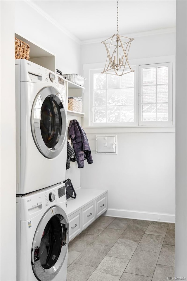 washroom with a notable chandelier, ornamental molding, and stacked washer and dryer