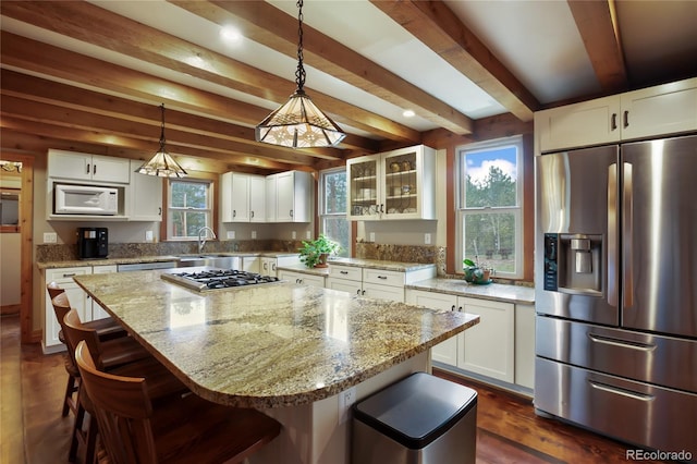 688 Obsidian Dr, Florissant, CO 80816 - kitchen with stainless steel appliances, beam ceiling, light stone counters, a breakfast bar, and white cabinetry