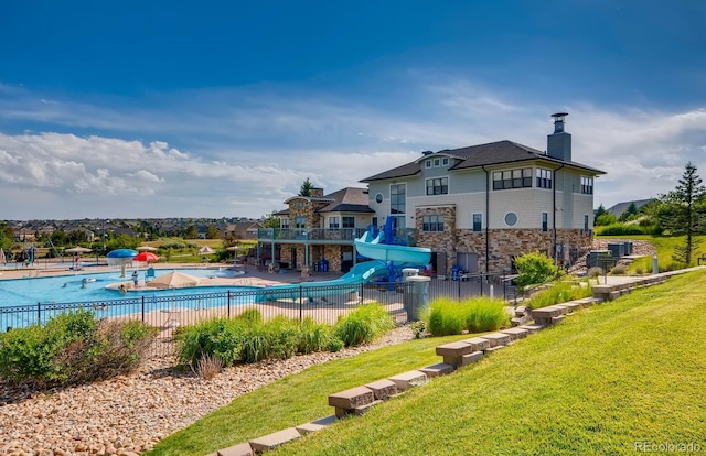 pool with a patio area, fence, a water slide, and a yard