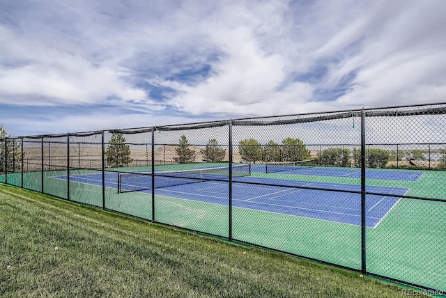 view of tennis court with a yard and fence