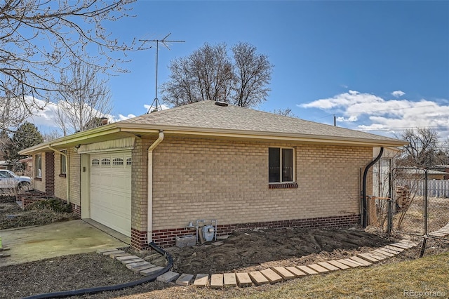 view of home's exterior with driveway, roof with shingles, an attached garage, fence, and brick siding