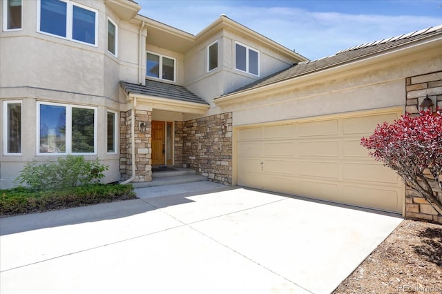 entrance to property featuring concrete driveway, stone siding, an attached garage, and stucco siding
