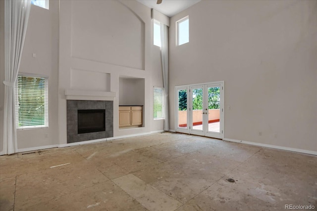 unfurnished living room featuring a towering ceiling, built in shelves, baseboards, french doors, and a fireplace