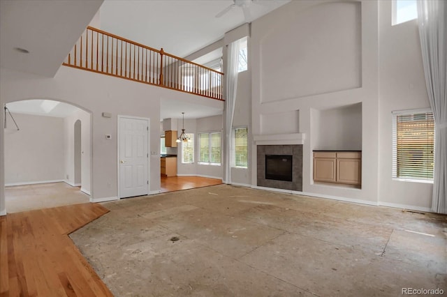 unfurnished living room with a high ceiling, a ceiling fan, baseboards, arched walkways, and a tiled fireplace