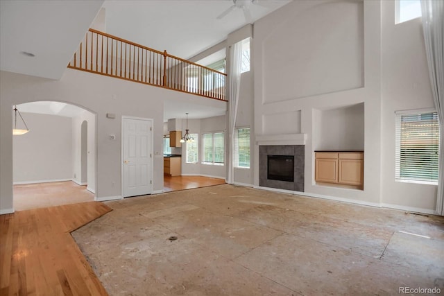 unfurnished living room with a high ceiling, ceiling fan, baseboards, a tiled fireplace, and arched walkways