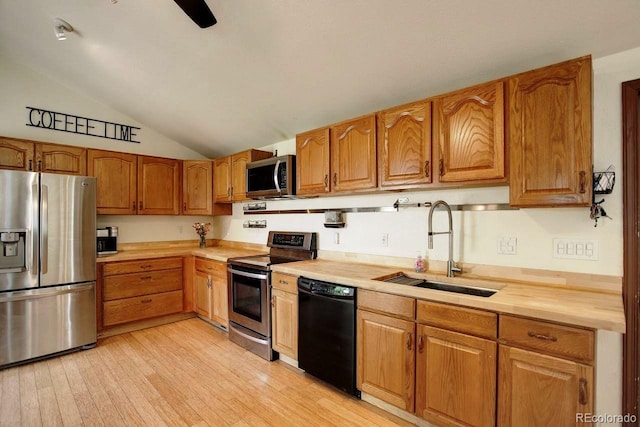 kitchen featuring appliances with stainless steel finishes, a sink, light countertops, lofted ceiling, and light wood finished floors