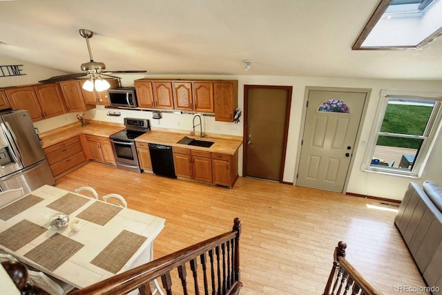 kitchen featuring stainless steel appliances, a sink, light countertops, a skylight, and a ceiling fan
