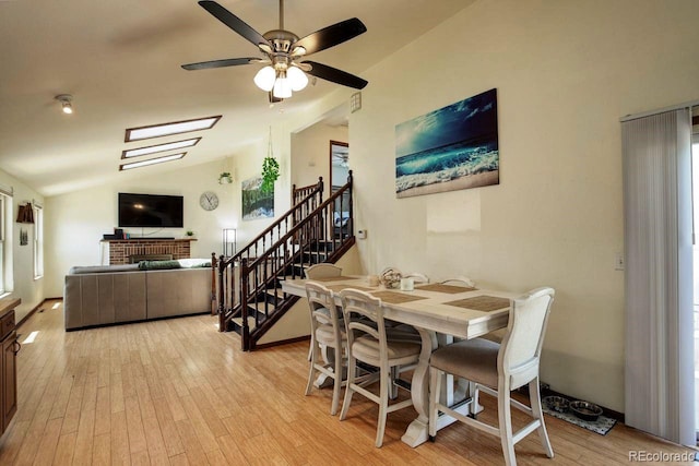 dining space featuring light wood-style floors, vaulted ceiling, ceiling fan, stairs, and a brick fireplace