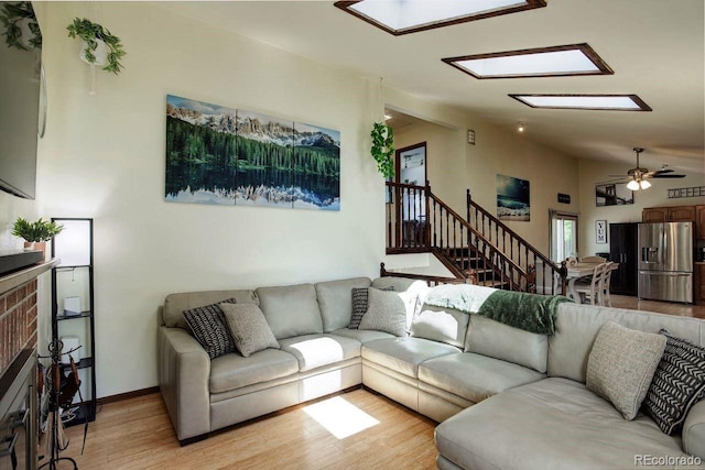 living area featuring light wood finished floors, lofted ceiling, a ceiling fan, stairs, and a skylight