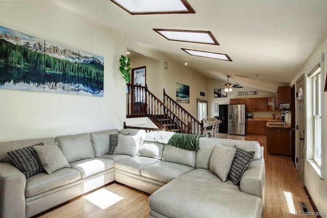 living area with lofted ceiling, light wood-style flooring, ceiling fan, and stairs