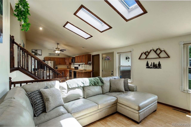 living area featuring a skylight, vaulted ceiling, light wood finished floors, stairs, and baseboards