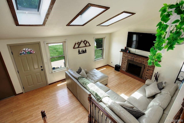 living area with a skylight, light wood-style floors, a brick fireplace, and vaulted ceiling