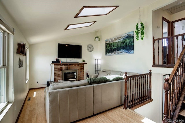 living room with light wood-type flooring, lofted ceiling, a fireplace, and stairway
