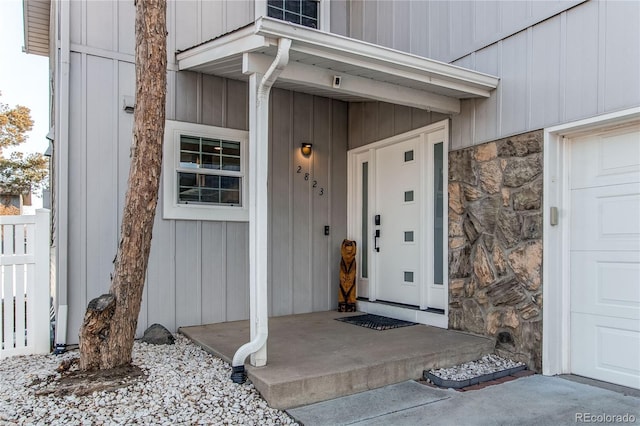 view of exterior entry with board and batten siding, a garage, and stone siding