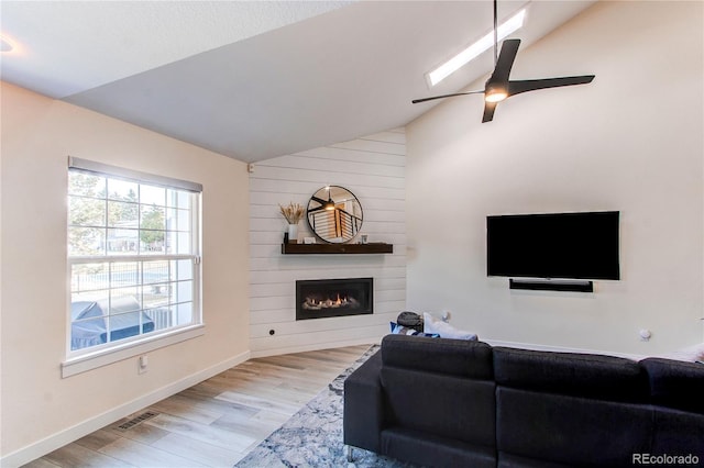 living area featuring wood finished floors, visible vents, baseboards, lofted ceiling, and a large fireplace