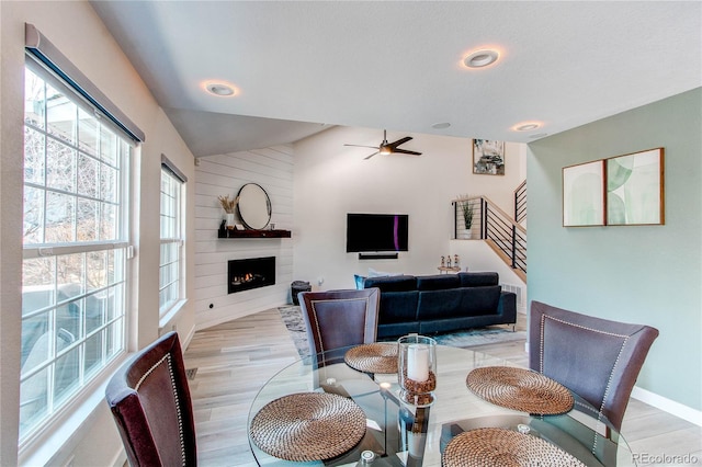 dining space featuring light wood finished floors, ceiling fan, stairs, lofted ceiling, and a fireplace