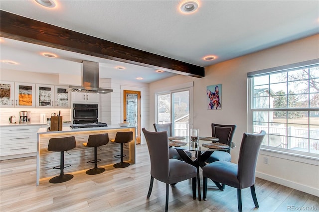 dining area with light wood-type flooring, beamed ceiling, baseboards, and a healthy amount of sunlight