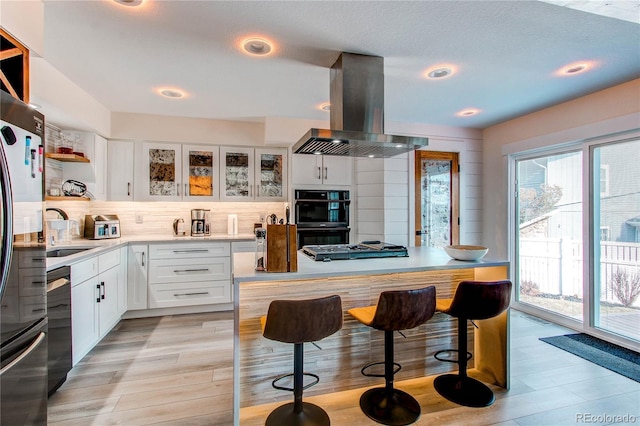 kitchen featuring dobule oven black, a sink, freestanding refrigerator, island range hood, and dishwashing machine